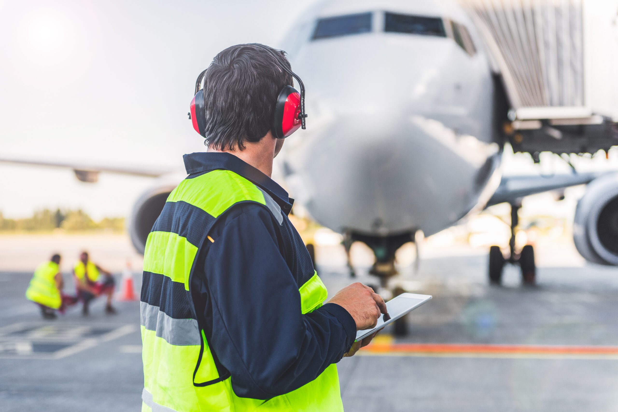 Technical staff wearing headset while checking plane. He typing notes in electronic tablet. He turning back to camera
